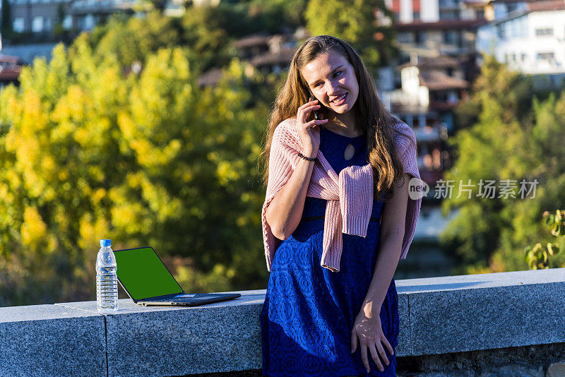 A young woman is talking on the phone outside, against the backdrop of the city.